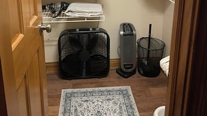 Habitación compacta con cama, una pequeña zona de estar, ventilador, calefacción y estanterías ordenadas.
