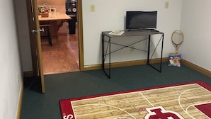 Una habitación con alfombra de canasta de baloncesto, un televisor sobre un mueble bajo y una puerta que da a otra habitación.