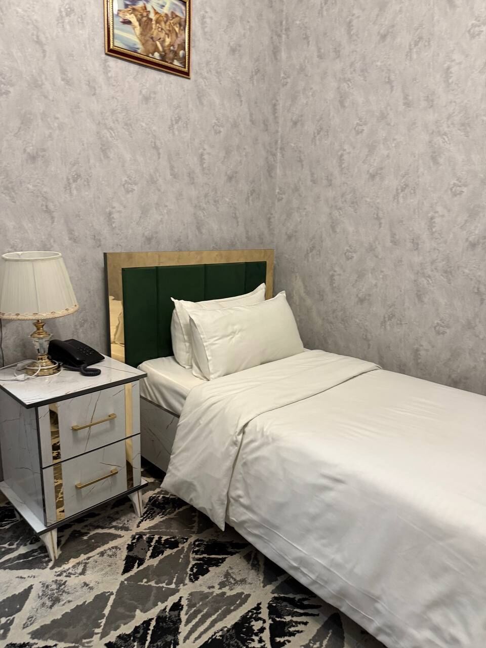 Habitación de hotel con cama, mesita de noche con lámpara, teléfono y un cuadro en la pared.