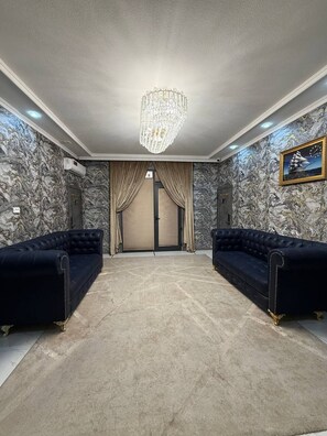 A room with a chandelier, two sofas, a patterned wall, and a door with curtains. - Royal Hotel Navoi (Navoiy)