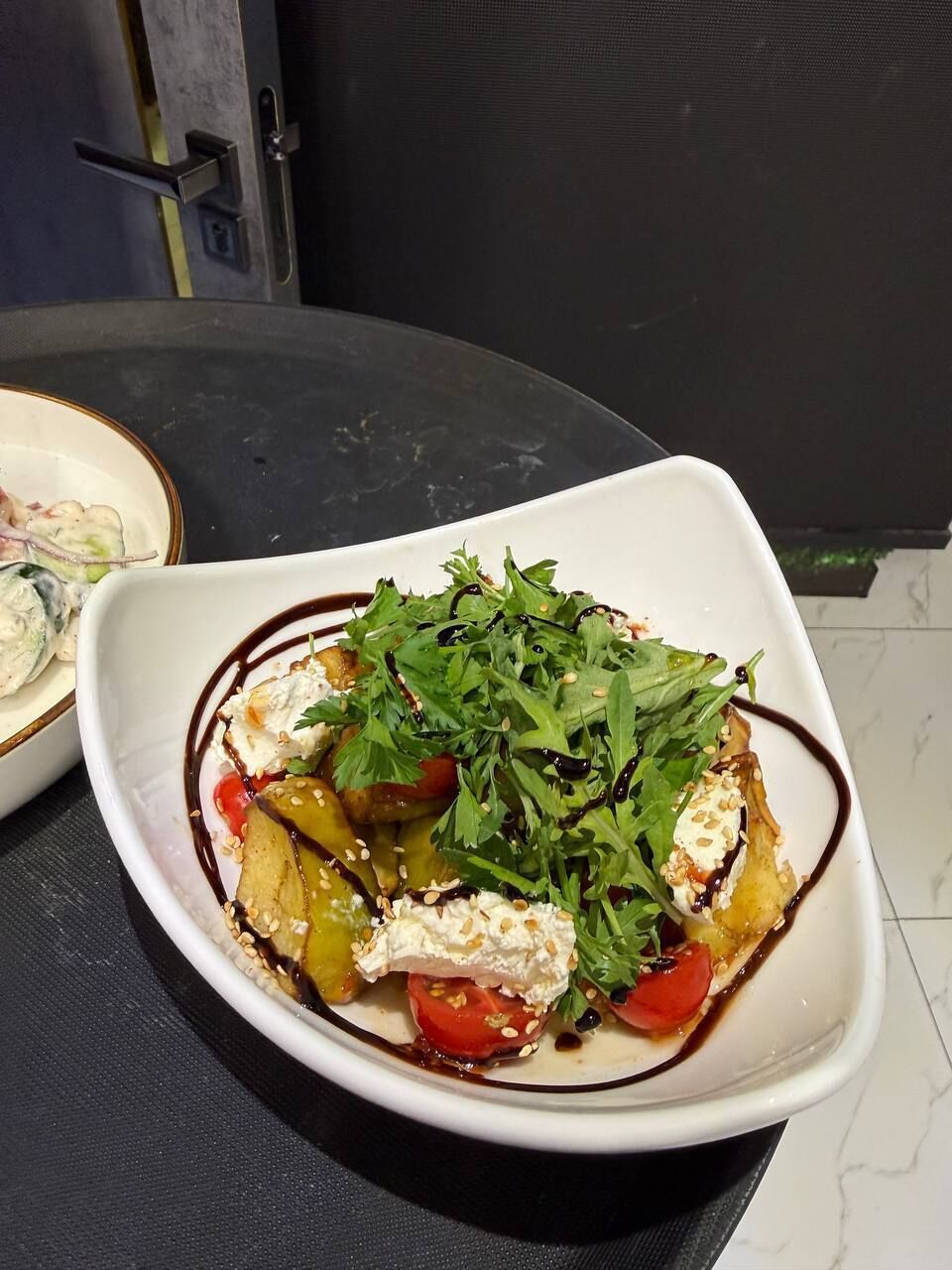 Un saladier blanc contenant une salade, posé sur une surface sombre.