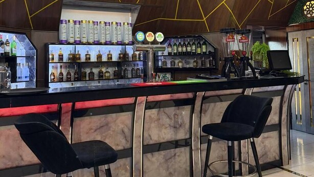 A bar area with a curved counter, hanging lights, and a selection of bottled beverages. - Royal Hotel Navoi (Navoiy)
