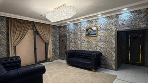A spacious living room with a chandelier, a black sofa, a black armchair, a marble-patterned wall, and a door with a golden handle. - Royal Hotel Navoi (Navoiy)