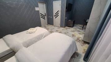 Una habitación de hotel con dos camas, una mesita, un televisor y un armario.
