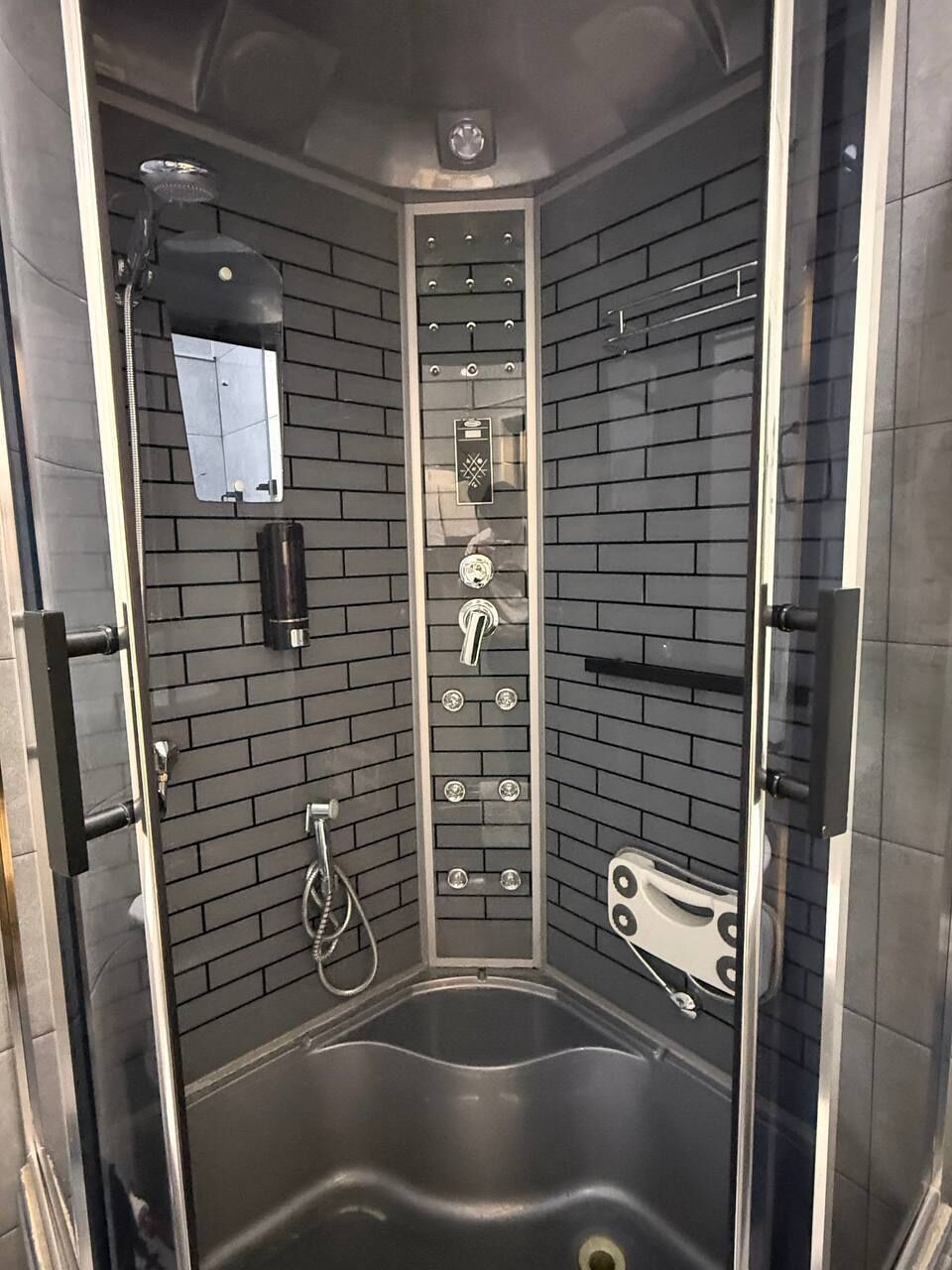 Un box de ducha moderno con puerta de cristal, un panel de control con varios botones y un cabezal de ducha manual.
