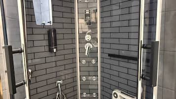 Un box de ducha moderno con puerta de cristal, un panel de control con varios botones y un cabezal de ducha manual.