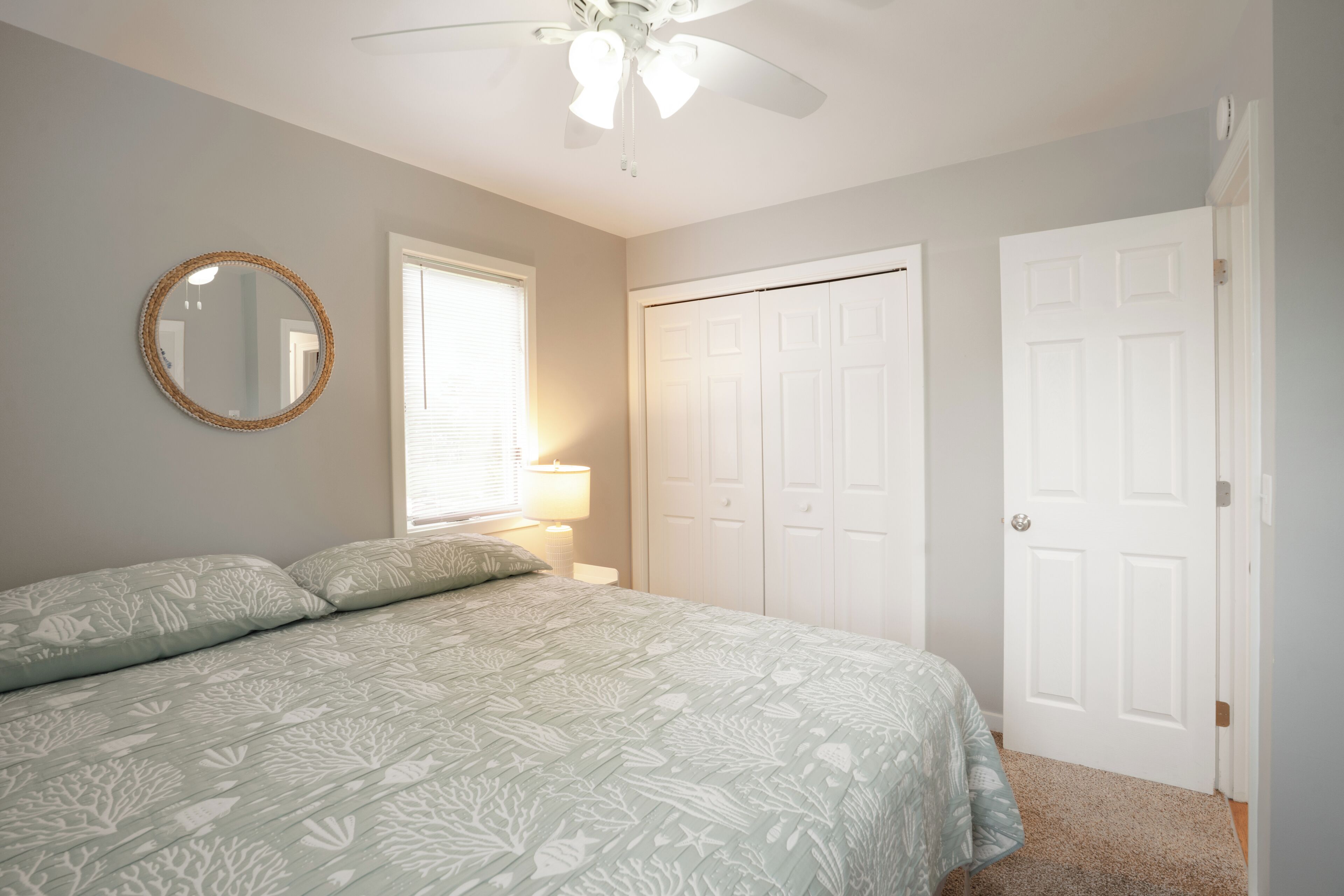 A bedroom with a bed, a round mirror, a ceiling fan, and a door.