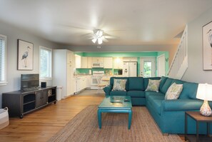 A modern living room with a teal sofa, a coffee table, and a TV. - Tideland Landing - Your 3 bedroom Ocracoke escape awaits (Ocracoke)