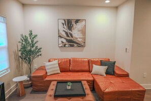 A living room with a leather sofa, a coffee table, a painting on the wall, and a potted plant. - Brand new Duplex in Cornelius convenient located (Cornelius)