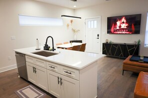 A modern kitchen with a central island, a dining area with chairs, a flat-screen TV mounted above the island, and a black console table with decorative items. - Brand new Duplex in Cornelius convenient located (Cornelius)