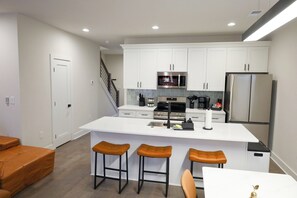 A modern kitchen with white cabinetry, a stainless steel refrigerator, a microwave, and a coffee maker. There are three stools at the island counter. - Brand new Duplex in Cornelius convenient located (Cornelius)