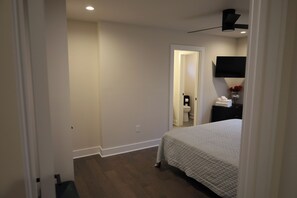 A bedroom with a bed, a flat-screen TV mounted on the wall, a bedside table with a vase of flowers, and a door leading to a bathroom. - Brand new Duplex in Cornelius convenient located (Cornelius)