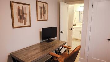 A room with a wooden desk, a black monitor, two framed abstract paintings, and a brown chair.