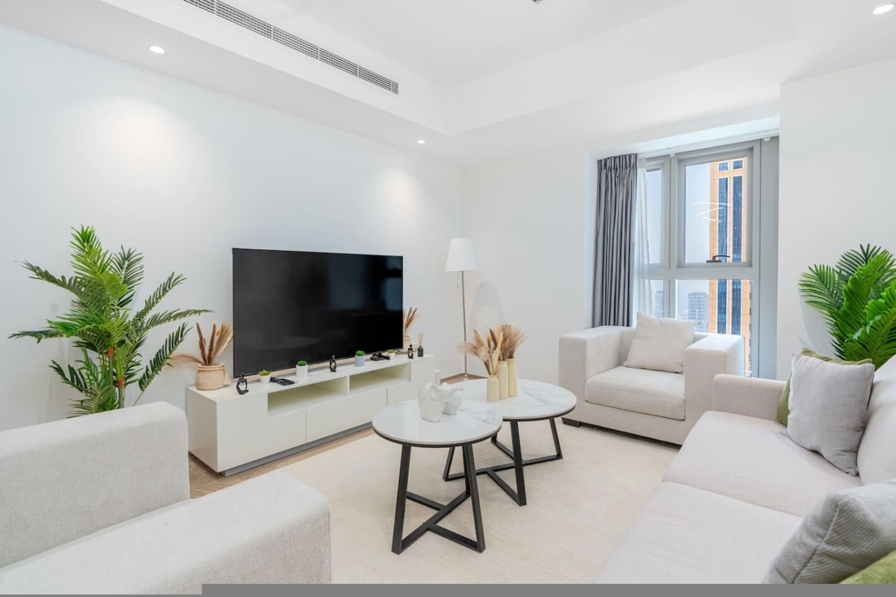 Ein stilvolles Wohnzimmer mit Flachbildfernseher, zwei Sofas, einem Couchtisch und Topfpflanzen.
