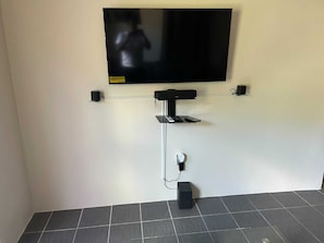 A flat-screen TV mounted on a wall with a cable management system, a remote control holder, and a speaker on the floor. - Relaxed Island Living Cottage (Annas Retreat)