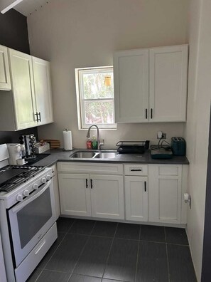 A kitchen with white cabinets, a stove, a sink, and a window. - Relaxed Island Living Cottage (Annas Retreat)