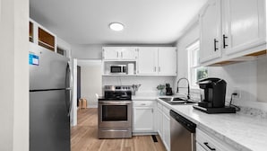 A modern kitchen with white cabinetry, stainless steel appliances, and a marble countertop.