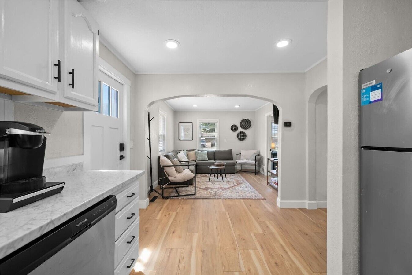 A modern kitchen with a coffee maker, a dining area with a sofa and chairs, and a refrigerator.