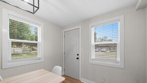 A room with a wooden floor, a white door, and two windows with blinds.