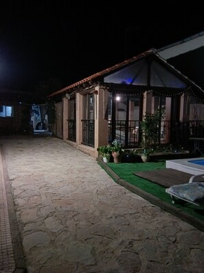 Pátio com piso de pedra, área coberta com assentos, plantas em vasos e uma piscina.