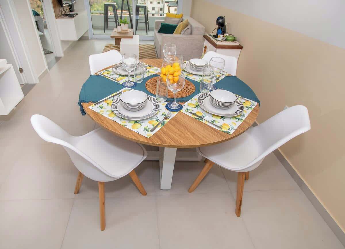 A dining area with a round table set for four, white chairs, and a view of the outdoors.