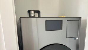 Un appareil combiné lave-linge et sèche-linge à chargement frontal, compact et fabriqué en acier inoxydable, doté d’un panneau de commande et d’un petit compartiment de rangement.