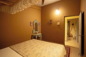 A bedroom with a bed, a dresser, a mirror, and a door leading to another room. - Heritage Haven (Ashwem)