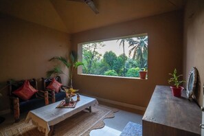 A room with a large window, a sofa, a table, and various plants. - Heritage Haven (Ashwem)