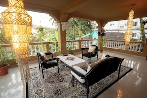 A covered outdoor seating area with a table and chairs, potted plants, and hanging lamps. - Heritage Haven (Ashwem)