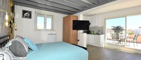 Un dormitorio con cama, televisión, ventana y balcón con mobiliario exterior.