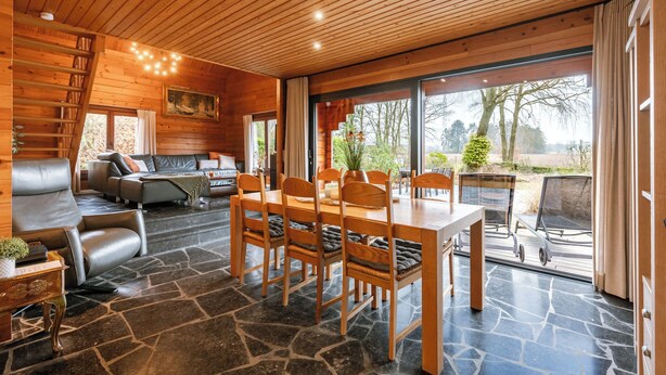 A wooden interior with a dining table, chairs, a sofa, and a staircase.