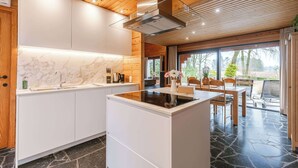 A modern kitchen with a central island, wooden ceiling, and large windows.
