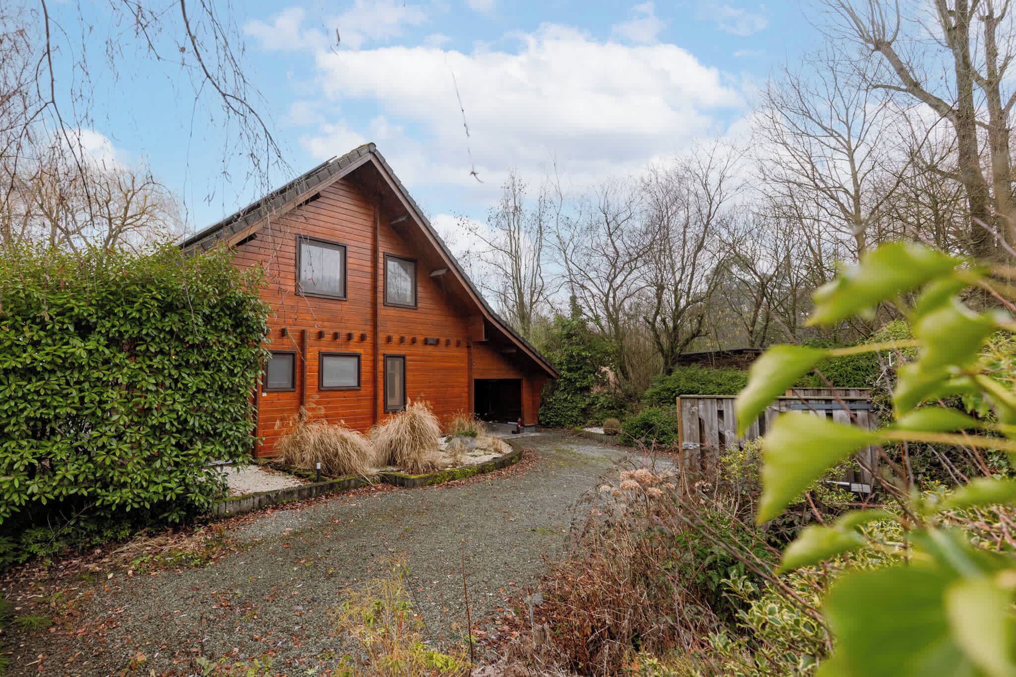 A wooden house with a sloped roof, surrounded by dense shrubbery and trees.