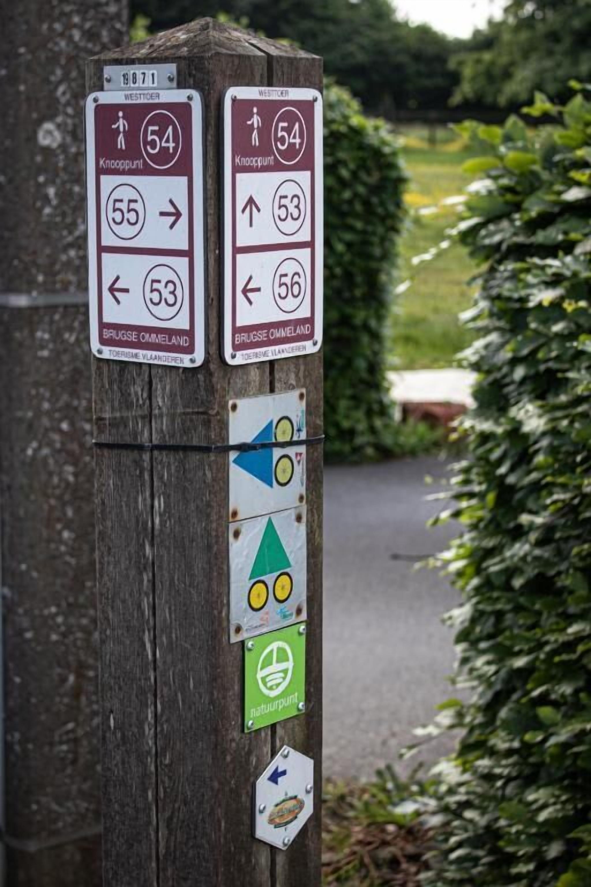 A wooden post with directional signs and symbols indicating routes and points of interest.