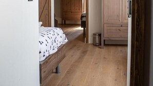 Une chambre avec un plancher en bois, un lit recouvert d’une couvre-lit à motifs, un luminaire suspendu et une armoire.
