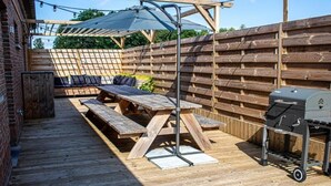 Une terrasse extérieure avec des bancs en bois, un barbecue et une pergola décorée de guirlandes lumineuses.