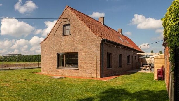 Une maison de plain-pied en briques, avec un toit en pente, une grande fenêtre et un petit garage attenant.