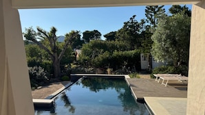 Une piscine dotée d’une terrasse en bois et de chaises longues, entourée d’arbres et surplombée par un ciel dégagé.