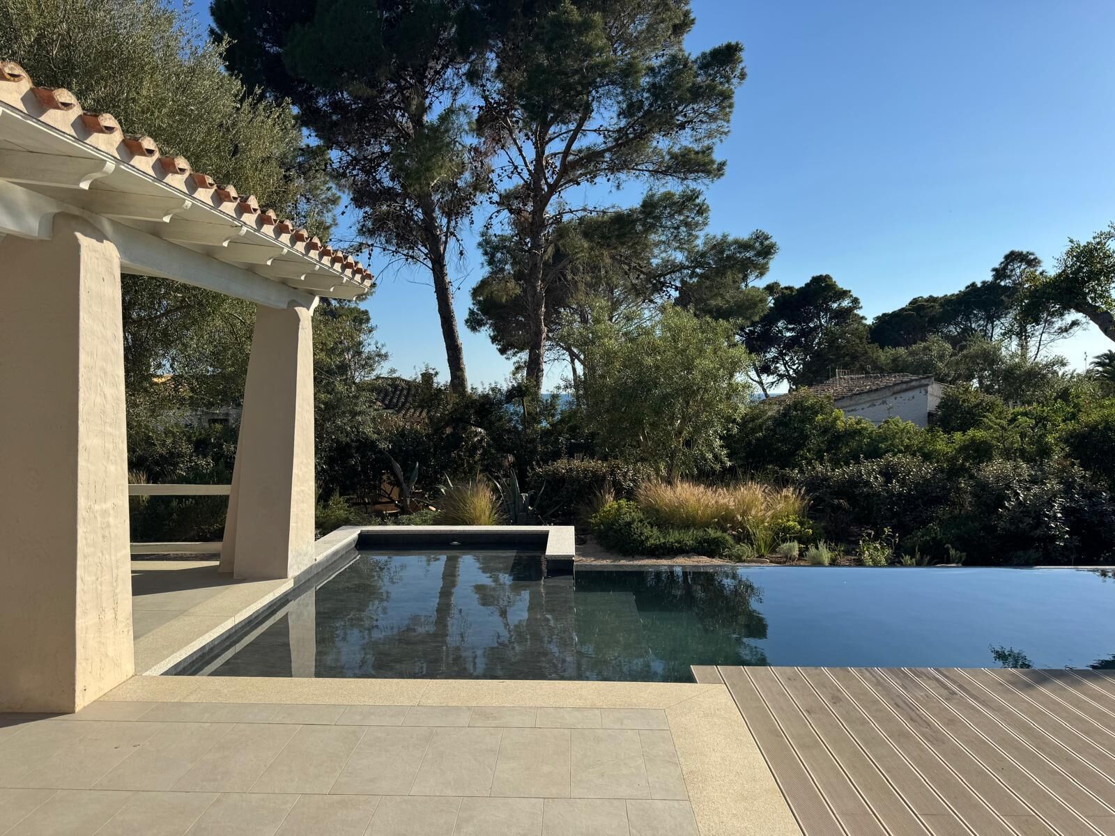A swimming pool with a pergola, surrounded by trees and a clear sky.