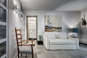 A modern living room with a white sofa, a wooden chair, a painting, and a lamp on a side table. - House Among the Olive Trees (villasimius)