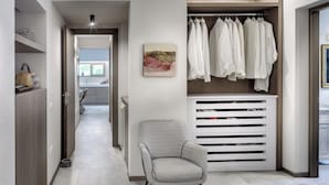 Un intérieur moderne avec un couloir menant à une cuisine, un coin salon agrémenté d’un fauteuil à motifs et un meuble de rangement pour les vêtements, avec des étagères pour suspendre les vêtements.