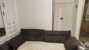 Un sofá de color neutro con un plaid estampado, un control remoto y una puerta al fondo.