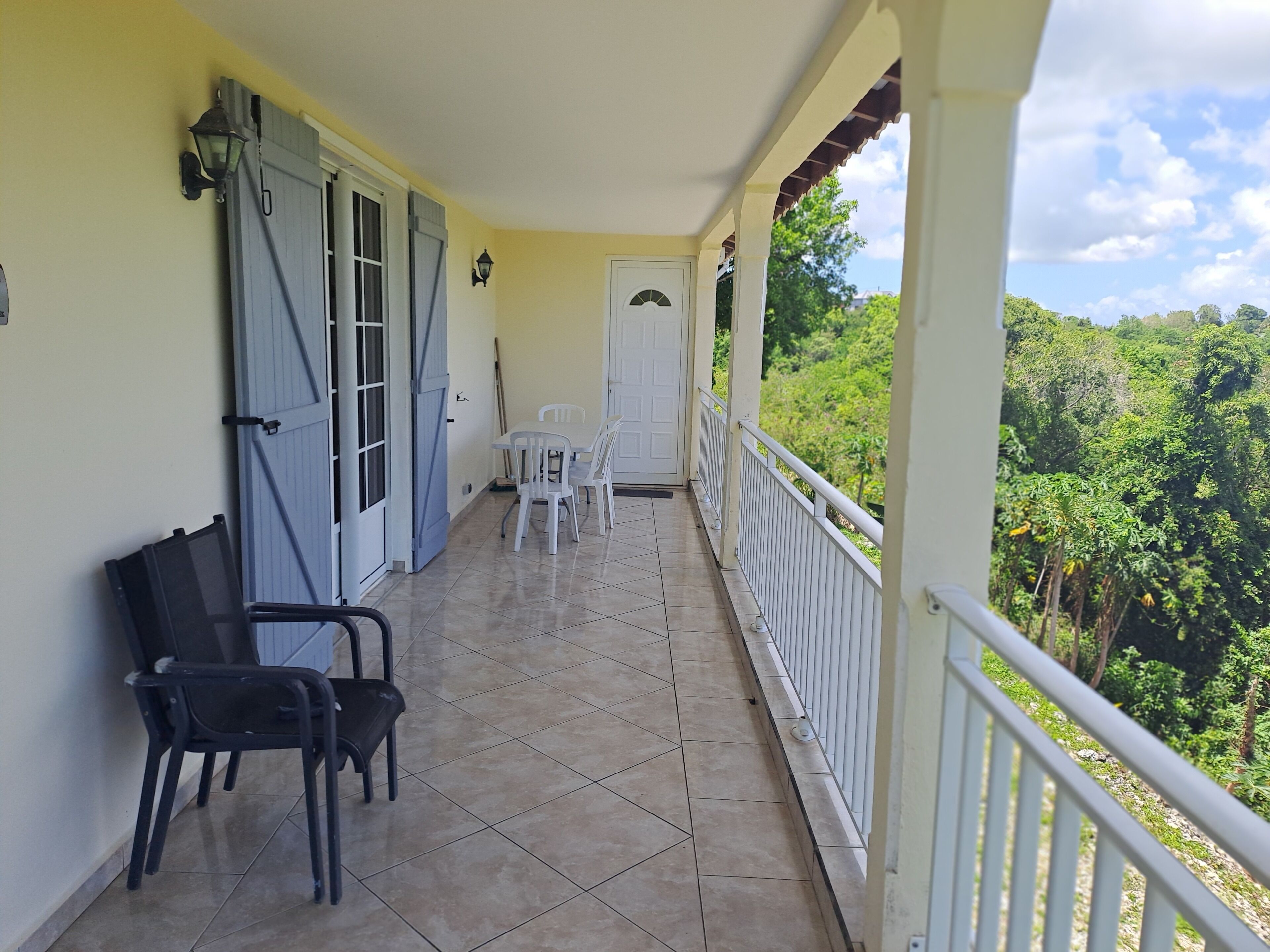 Un balcon doté d’un sol carrelé, d’une porte blanche et offrant une vue sur la verdure.