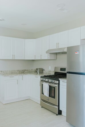 A kitchen with white cabinets, a stainless steel refrigerator, a gas stove, and a toaster. - Modern 2BR • Gated Parking • 10 Min to Downtown (Detroit)