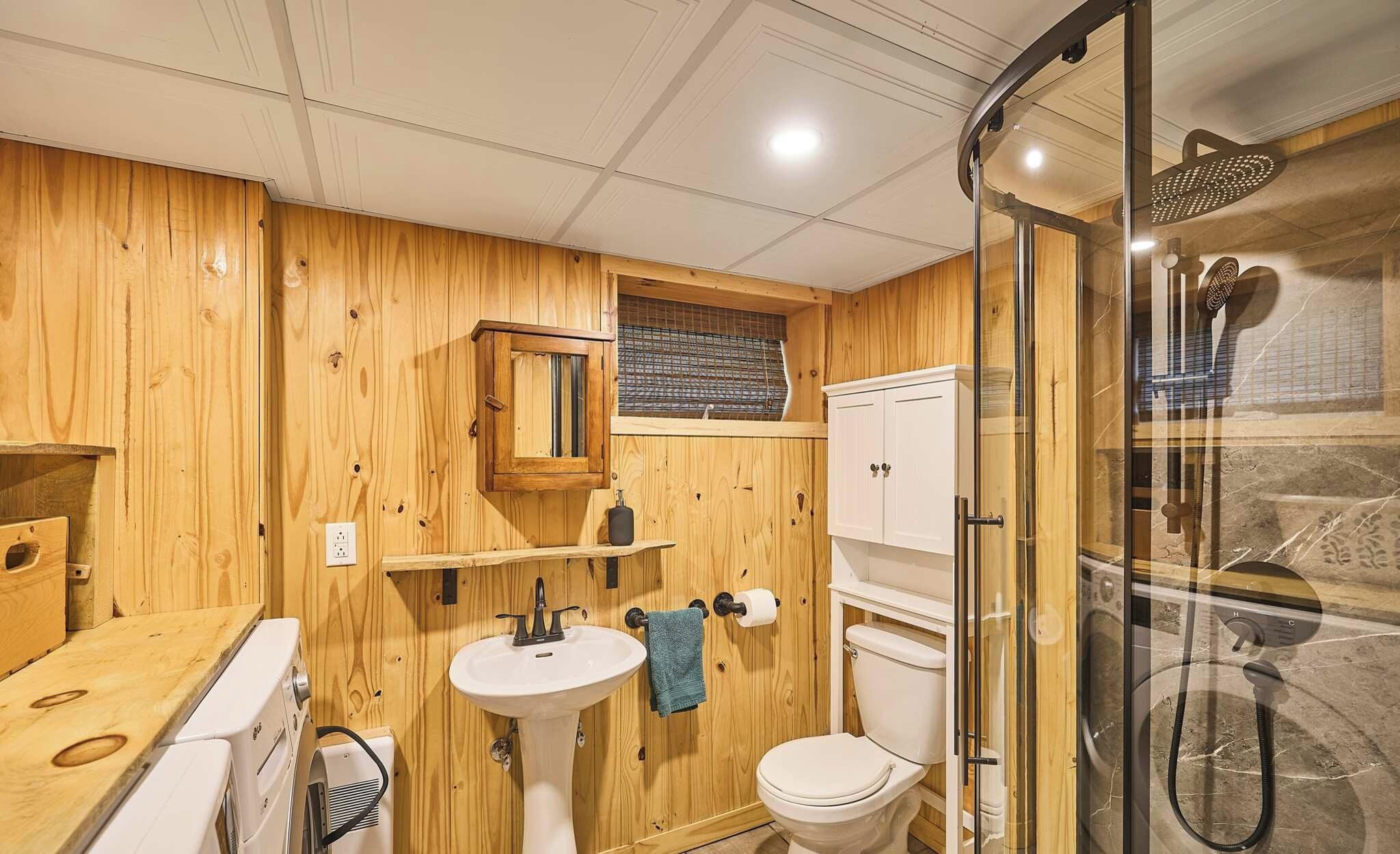 Une salle de bain aux murs lambrissés, dotée d’une douche à parois de verre, d’un lavabo blanc et de toilettes.