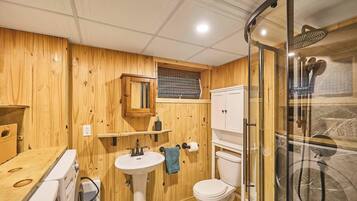 Une salle de bain aux murs lambrissés, dotée d’une douche à parois de verre, d’un lavabo blanc et de toilettes.