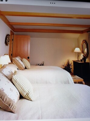 Un dormitorio con cama, almohadas, un armario de madera, una mesita de noche, una lámpara y un espejo.