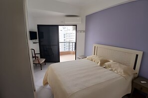 Un dormitorio con cama, una silla, un escritorio y un televisor.
