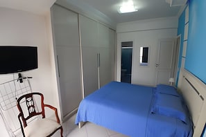 Un dormitorio con cama, armario, televisor y una silla.