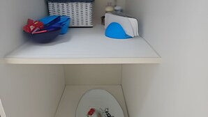 Een wit schap met een blauw-witte mand, een blauwe handdoek en een kleine witte schaal met een rood voorwerp.